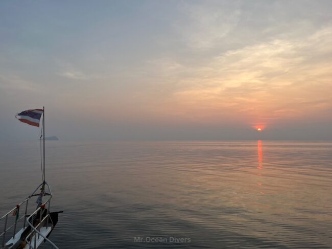 海を走行中の船の船首にあるタイ国旗とその先には朝日が出ています