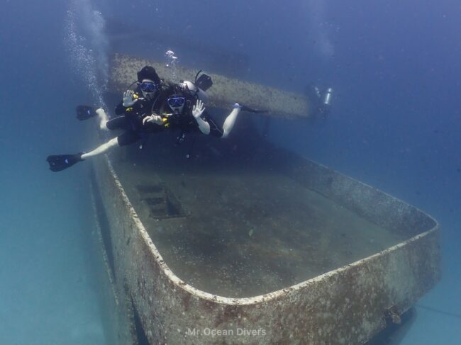 海に沈む沈船を背景に2人のダイバーがいます