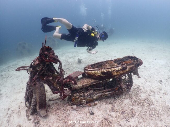 海の中に沈むスクーターの周りに1人のダイバーが浮かんでいます