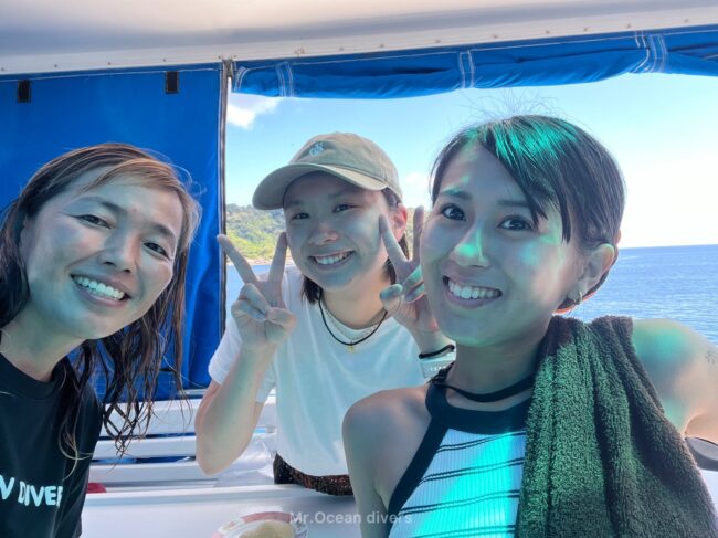空と海が見える背景で3人の女子が笑っています。