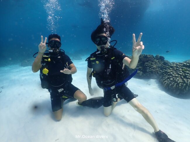 2人のダイバーが砂地に膝を付いてピースサインをしています