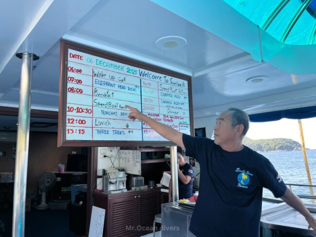 ホワイトボードに指を刺しながら説明をしている1人の男性が見えます