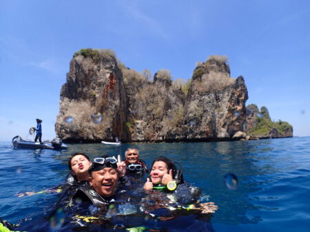 島を背景に4人のダイバーが海に浮いて笑っているのが見えます